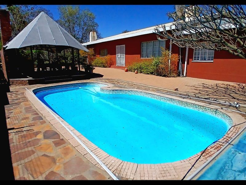Outdoor pool area featuring a swimming pool, paved patio, and a covered gazebo, set against the rear elevation of the house.