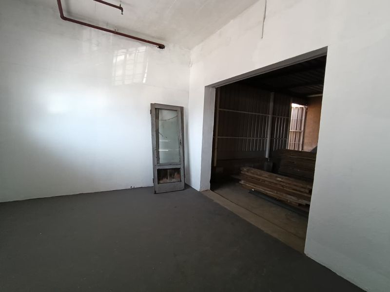 An industrial utility space featuring concrete flooring, exposed fire sprinkler piping, and a large open doorway leading to an adjacent storage area.