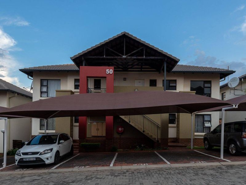 Front elevation of a townhouse complex featuring a tiled roof, covered parking bays, and an external staircase leading to upper-level units.
