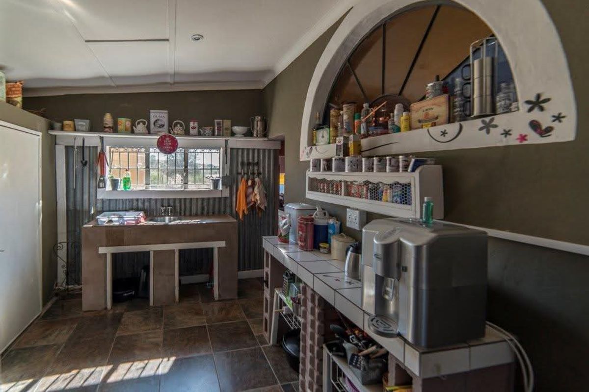 A rustic kitchen area featuring tiled countertops, a built-in sink, and unique arched wall shelving with corrugated metal wall accents.