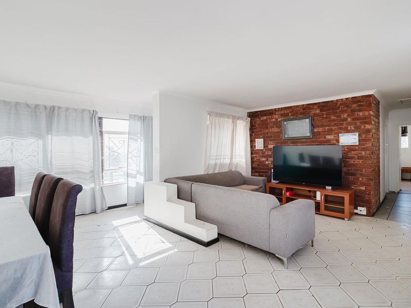 Open-plan living and dining area featuring a prominent exposed brick wall, ceramic tiled flooring, and a functional layout with natural light.