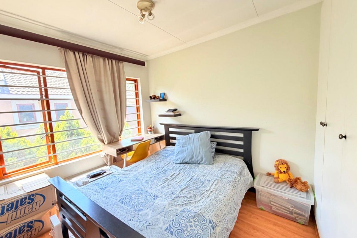 A functional bedroom featuring laminate flooring, a built-in wardrobe, and a window with security bars, offering natural light and practical storage space.