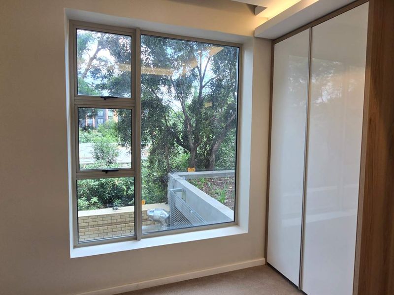 A bright, modern bedroom featuring a large window with exterior views and a sleek, built-in wardrobe with high-gloss finish.