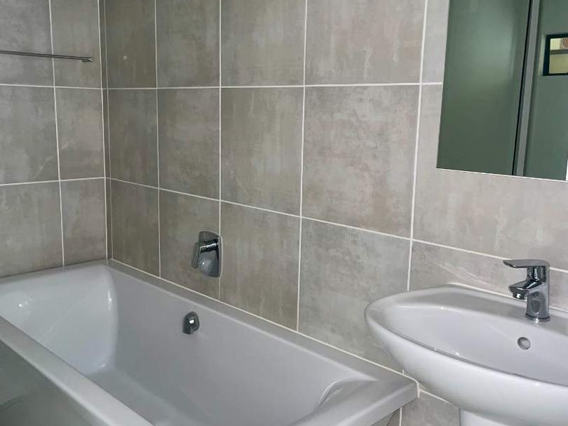 A clean, modern bathroom featuring a white bathtub, pedestal basin with mixer tap, and neutral wall tiling.