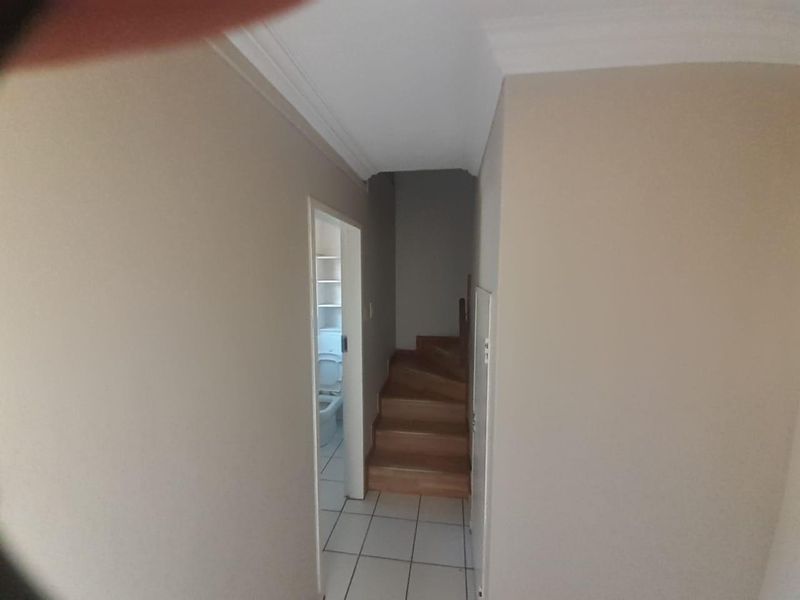 A functional hallway featuring tiled flooring and a staircase leading to the upper level, with a glimpse into an adjacent bathroom.