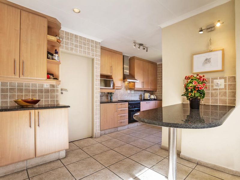 A functional kitchen featuring light wood cabinetry, granite countertops, tiled backsplash, and a convenient breakfast bar area with tiled flooring throughout.