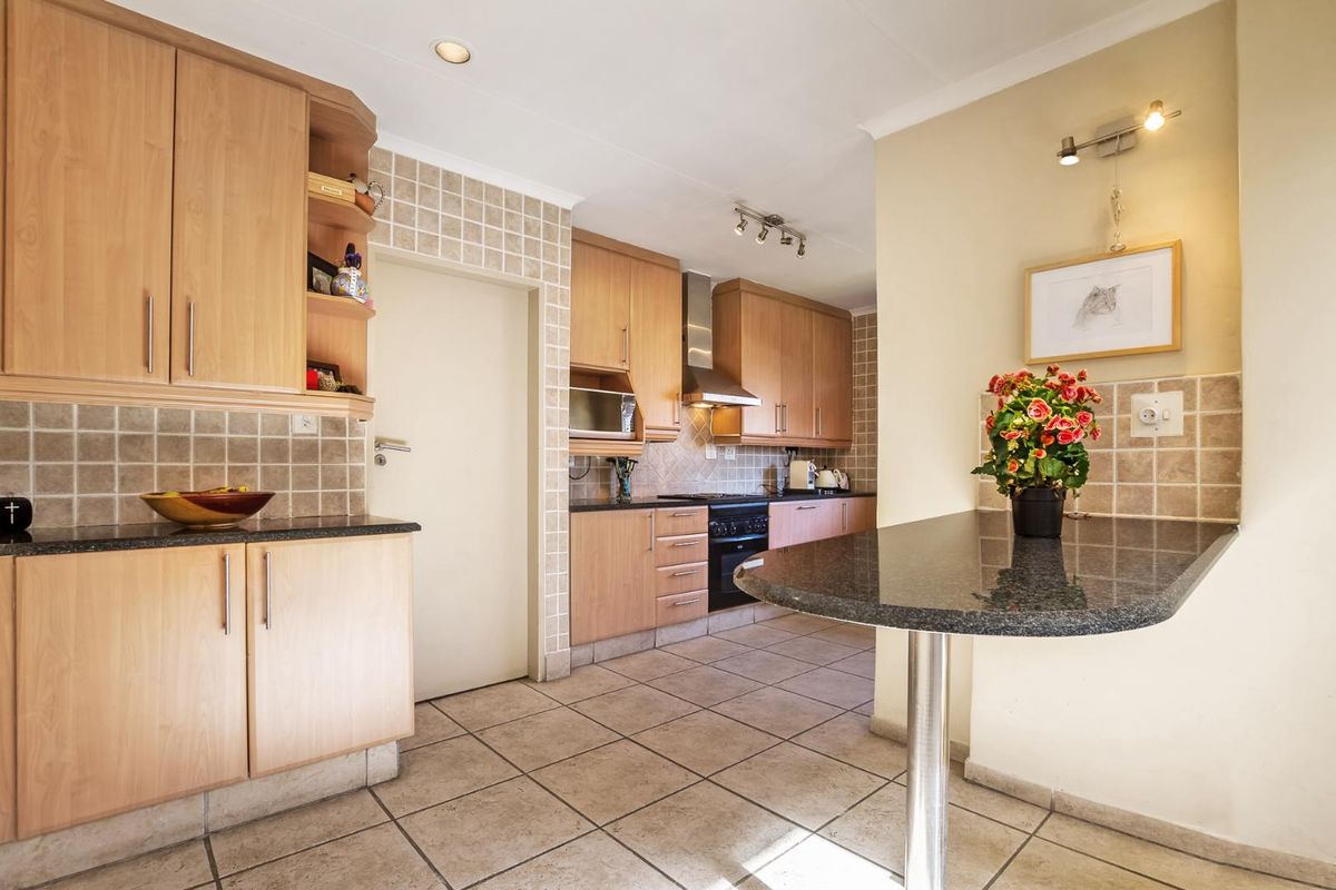 A functional kitchen featuring light wood cabinetry, granite countertops, tiled backsplash, and a convenient breakfast bar area with tiled flooring throughout.