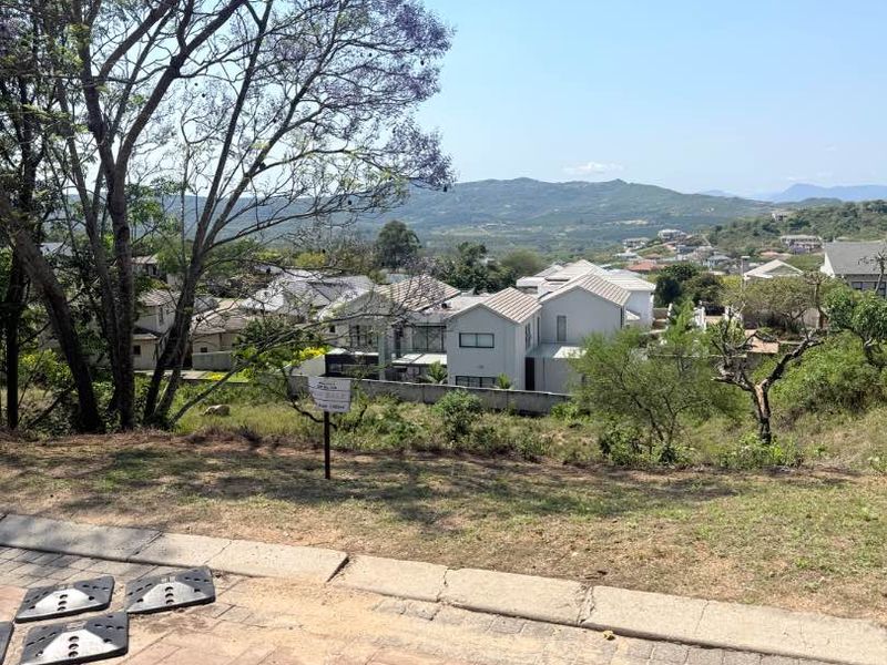 A view from a residential plot overlooking a suburban neighborhood with distant mountain scenery.