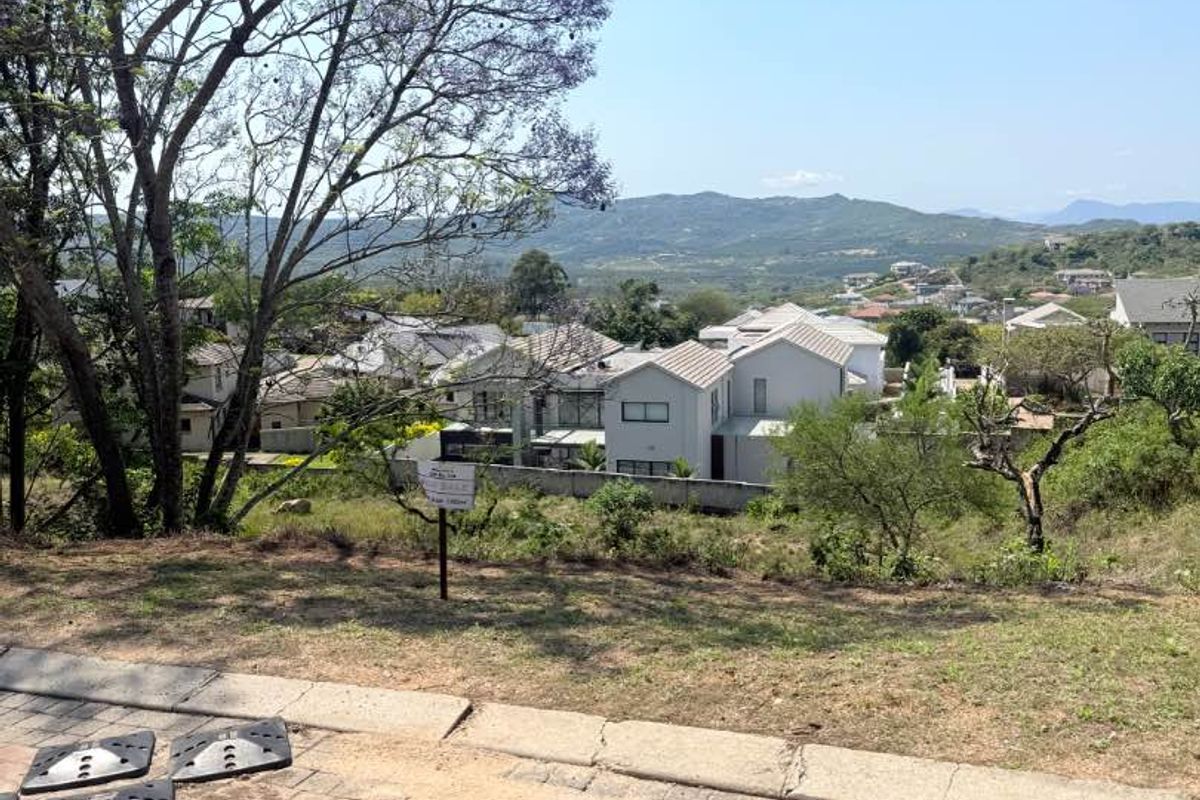 A view from a residential plot overlooking a suburban neighborhood with distant mountain scenery.