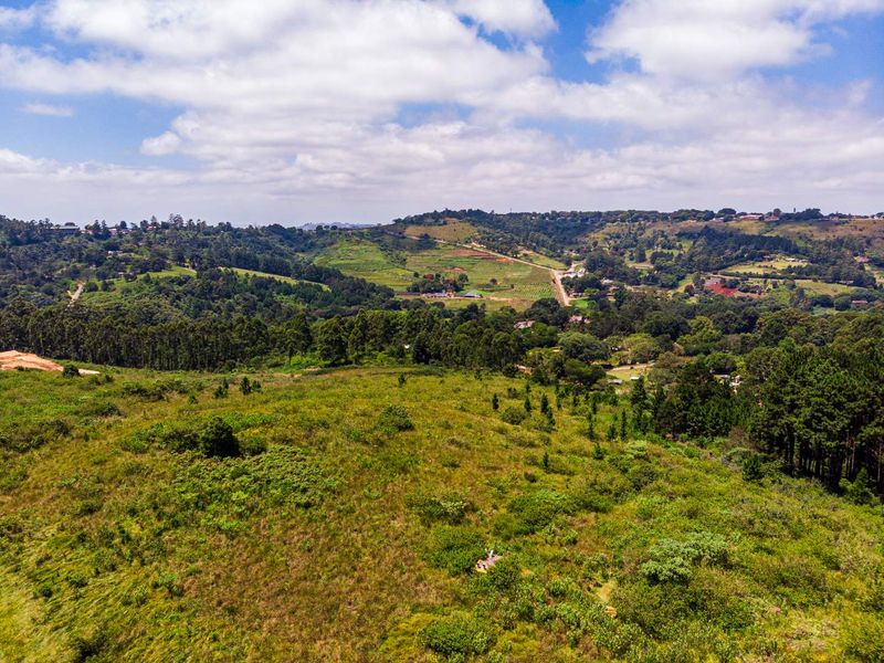 An aerial view of a large, undeveloped residential plot featuring rolling green hills, natural vegetation, and surrounding rural landscape.