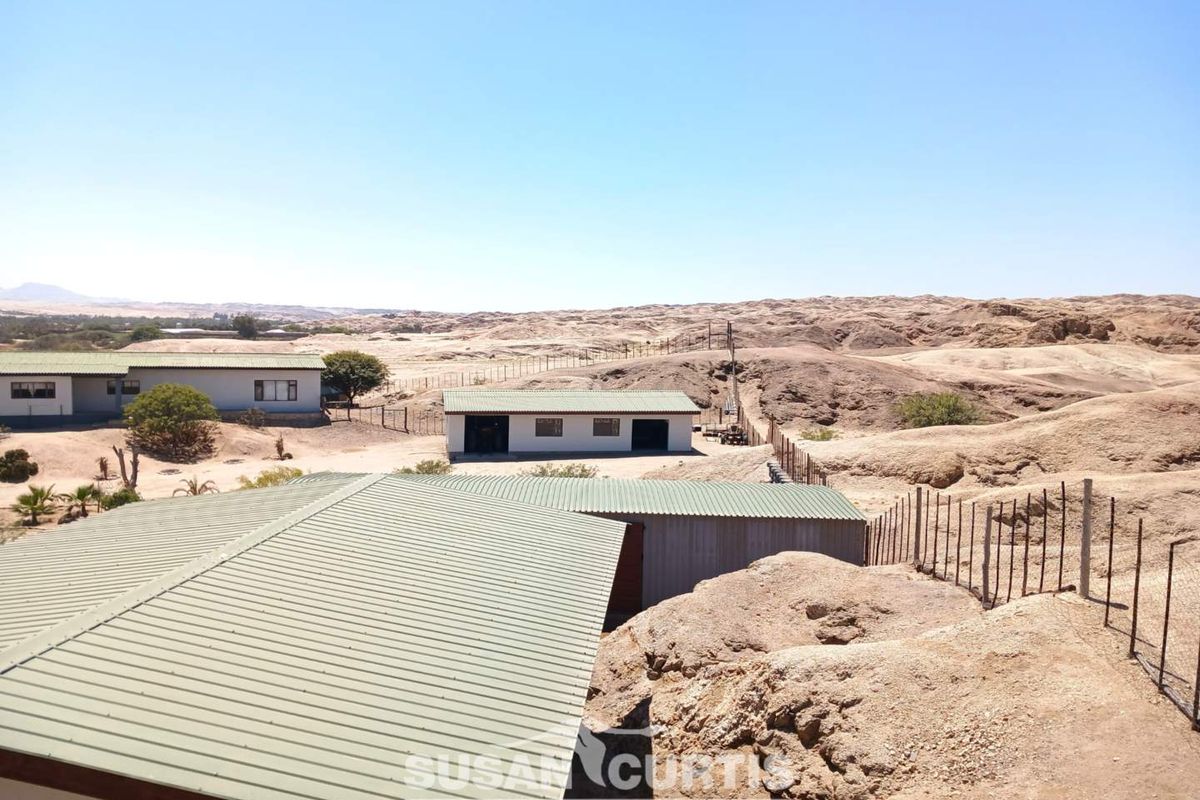 An elevated view of the small holding property, showcasing multiple outbuildings with corrugated metal roofing set within a rugged, arid landscape.