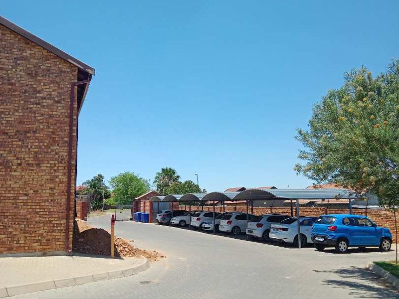 Exterior view of the apartment complex showing a brick building facade, paved driveway, and covered parking bays for residents.