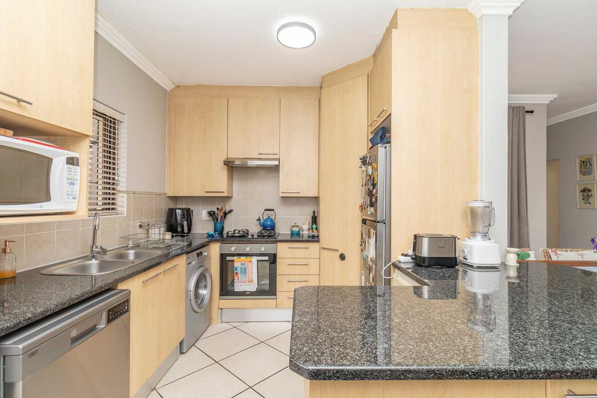 A functional kitchen featuring light wood cabinetry, granite countertops, a gas hob, built-in oven, and tiled flooring with an integrated laundry space.