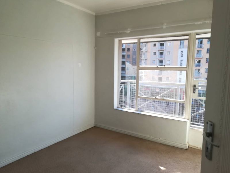 An empty bedroom featuring carpeted flooring, a large window, and direct access to a balcony.