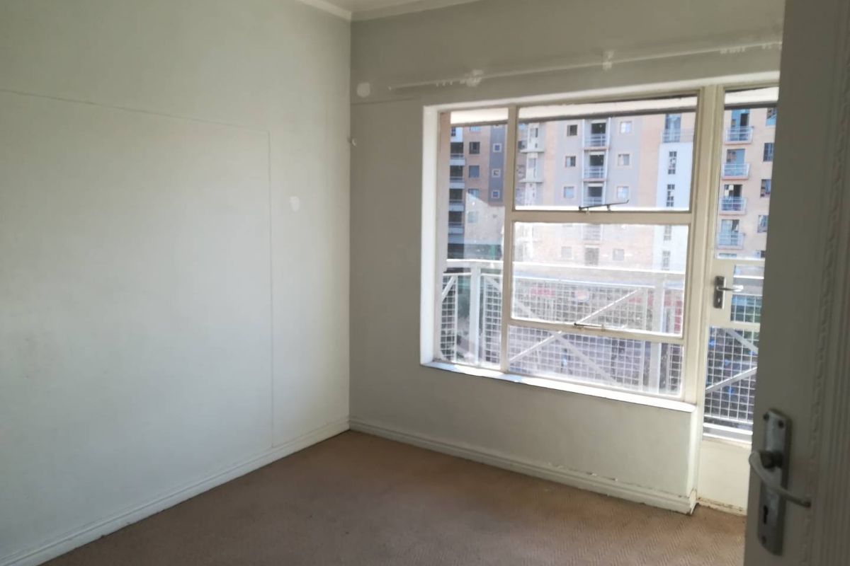 An empty bedroom featuring carpeted flooring, a large window, and direct access to a balcony.