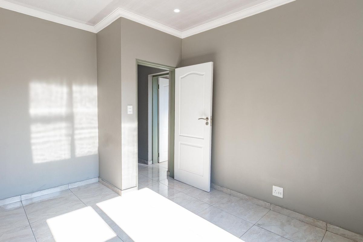 A bright, empty bedroom featuring neutral grey walls, tiled flooring, and recessed ceiling lighting, offering a clean and versatile living space.