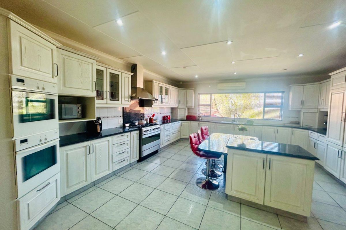 Spacious kitchen featuring white cabinetry, dark granite countertops, a central island, built-in double ovens, and a stainless steel extractor fan.