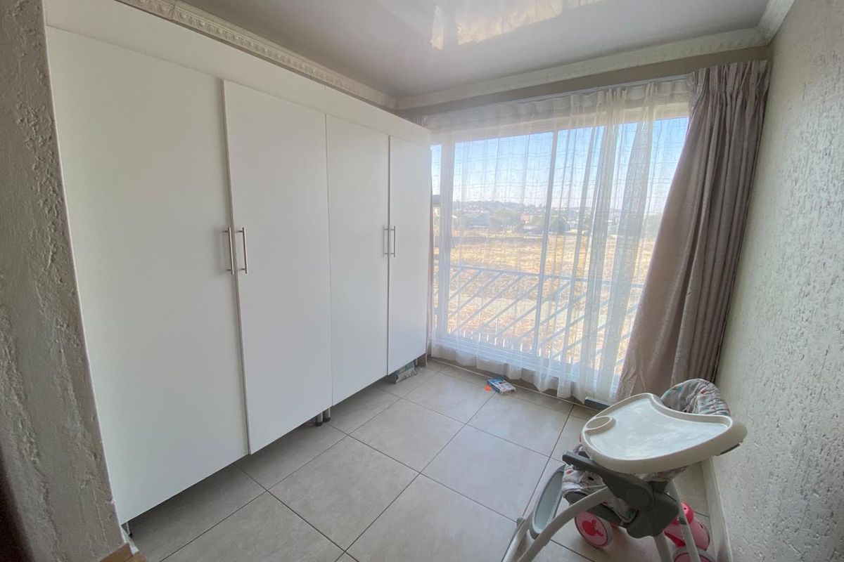 A bedroom featuring large built-in white wardrobes, tiled flooring, and a sliding glass door leading to a balcony with exterior views.