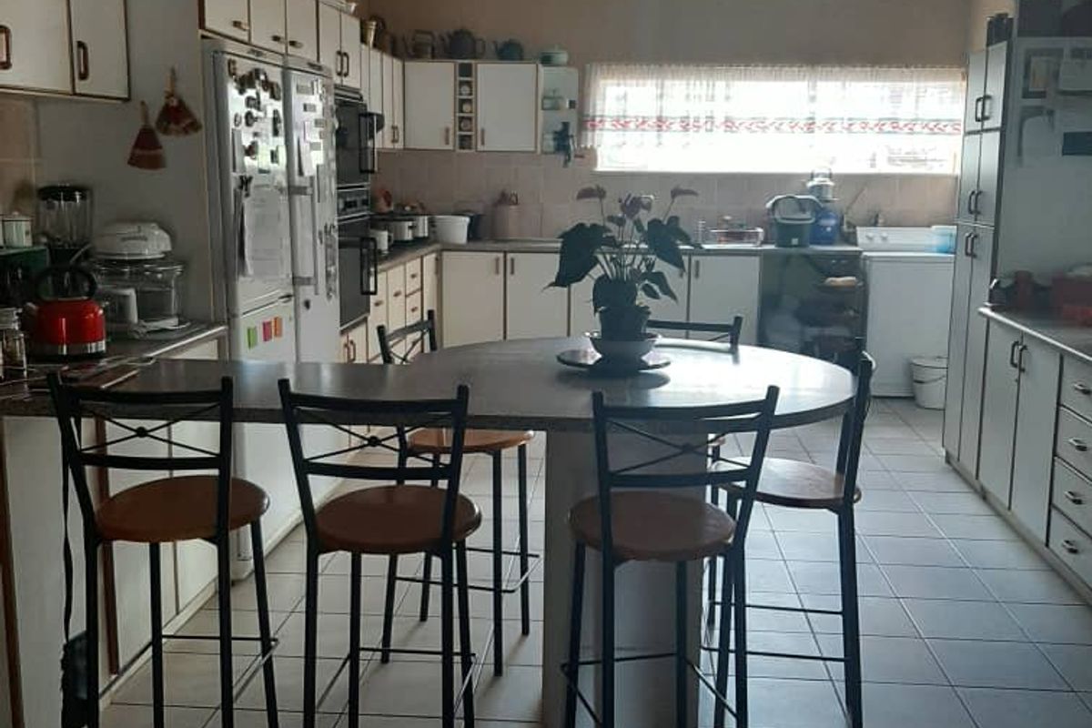 A spacious kitchen featuring extensive cabinetry, a central breakfast bar, and tiled flooring, offering a functional layout with potential for modern updates.
