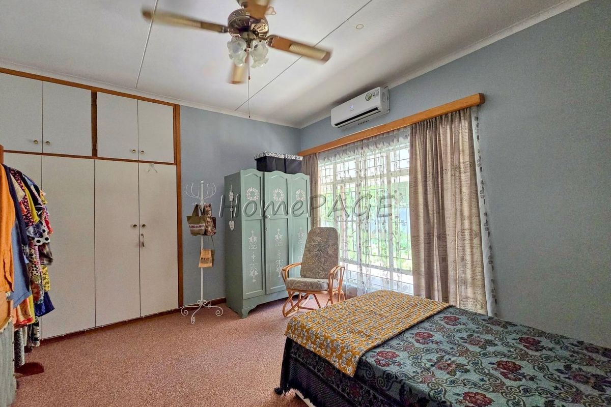 A bedroom featuring built-in cupboards, a ceiling fan, and a wall-mounted air conditioning unit, providing functional storage and climate control.