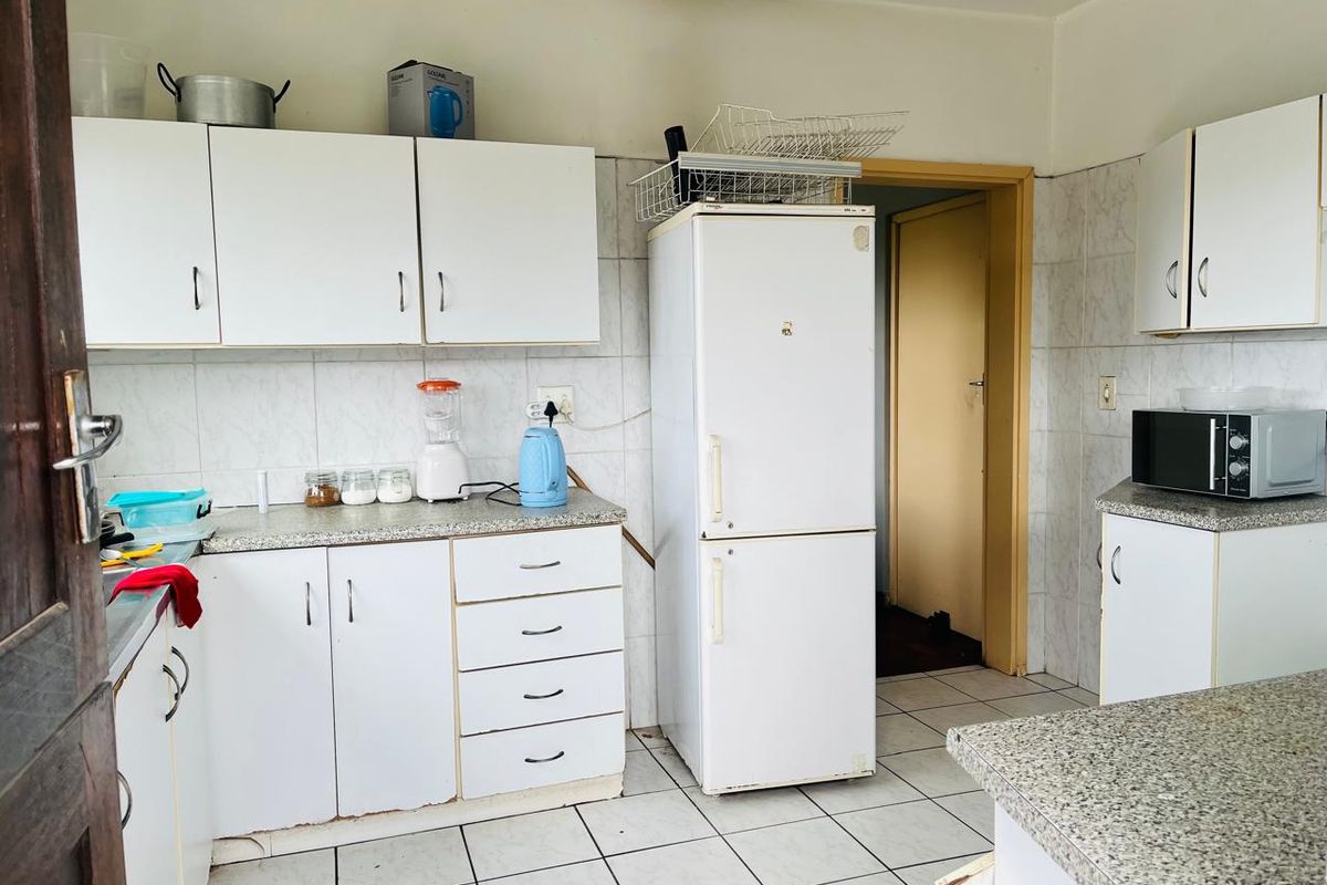 A functional kitchen featuring white cabinetry, laminate countertops, and tiled finishes, offering a dated aesthetic with potential for modernization.