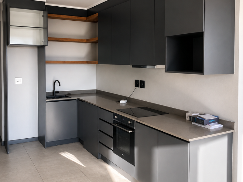 Modern kitchen featuring sleek dark grey cabinetry, stone countertops, integrated oven, electric hob, and open wooden shelving in a clean, contemporary apartment setting.