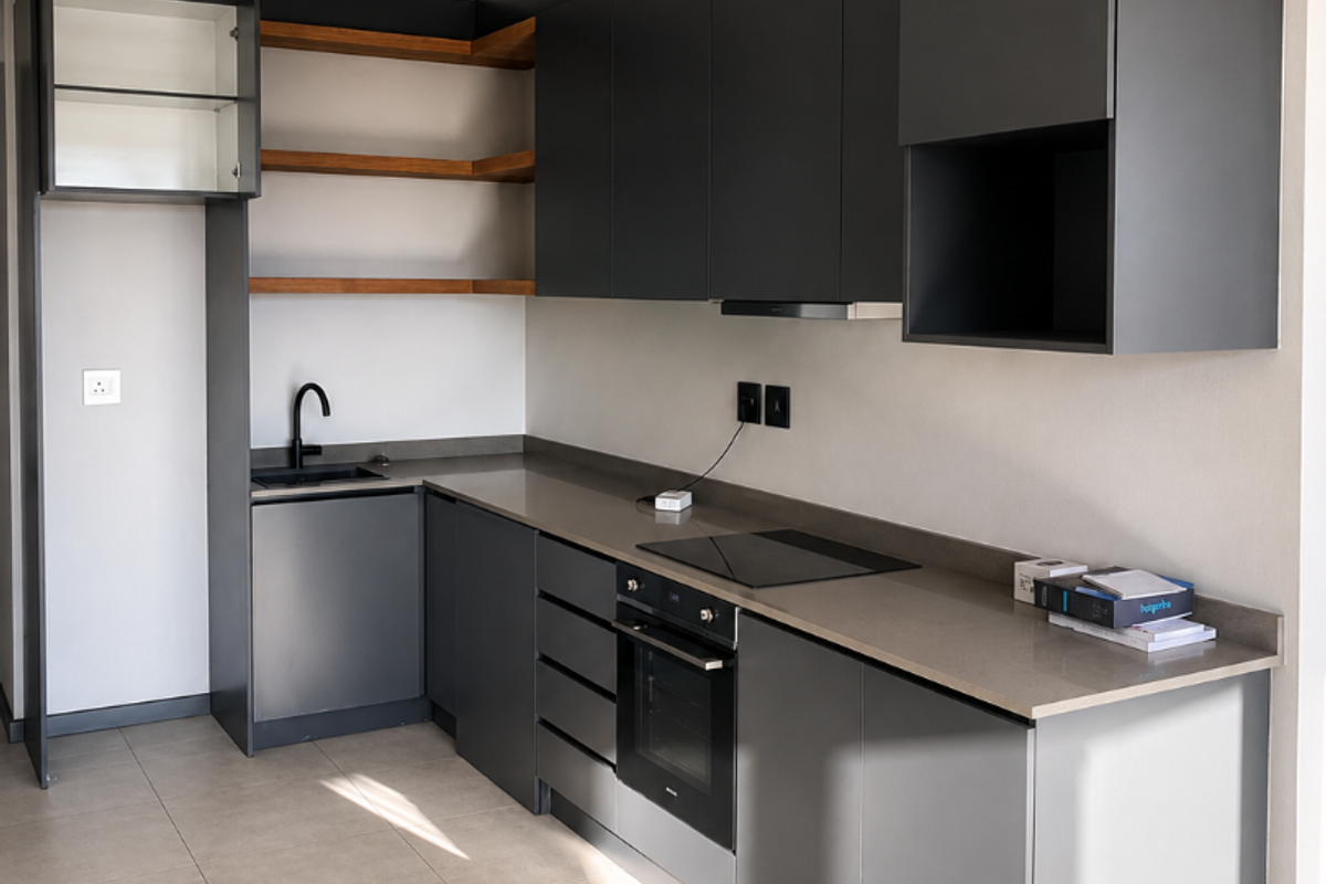 Modern kitchen featuring sleek dark grey cabinetry, stone countertops, integrated oven, electric hob, and open wooden shelving in a clean, contemporary apartment setting.