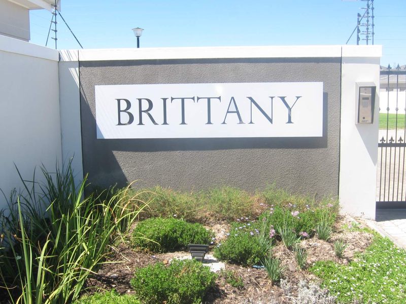Entrance to Brittany complex featuring a modern boundary wall, secure metal gate, intercom system, and well-maintained landscaped garden.