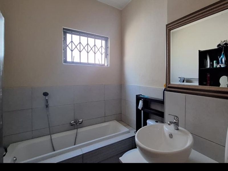 A functional bathroom featuring a bathtub with shower attachment, a modern basin, and a wall-mounted mirror, finished with neutral wall tiles.