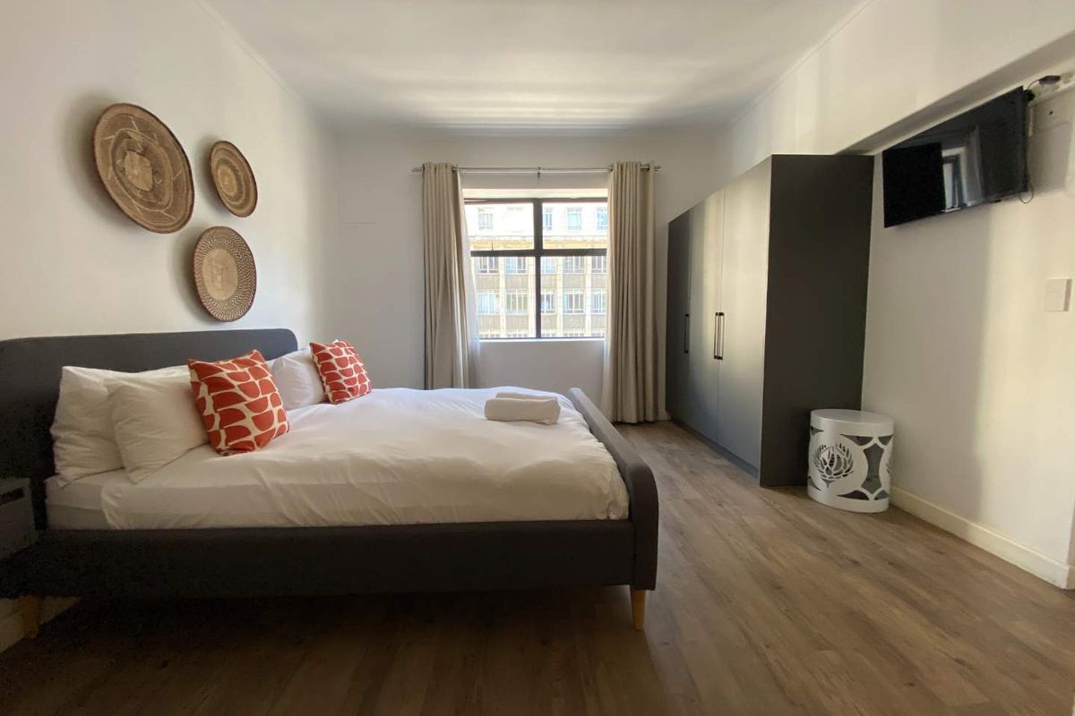 A well-maintained bedroom featuring modern laminate flooring, a large built-in wardrobe, and a window providing natural light.