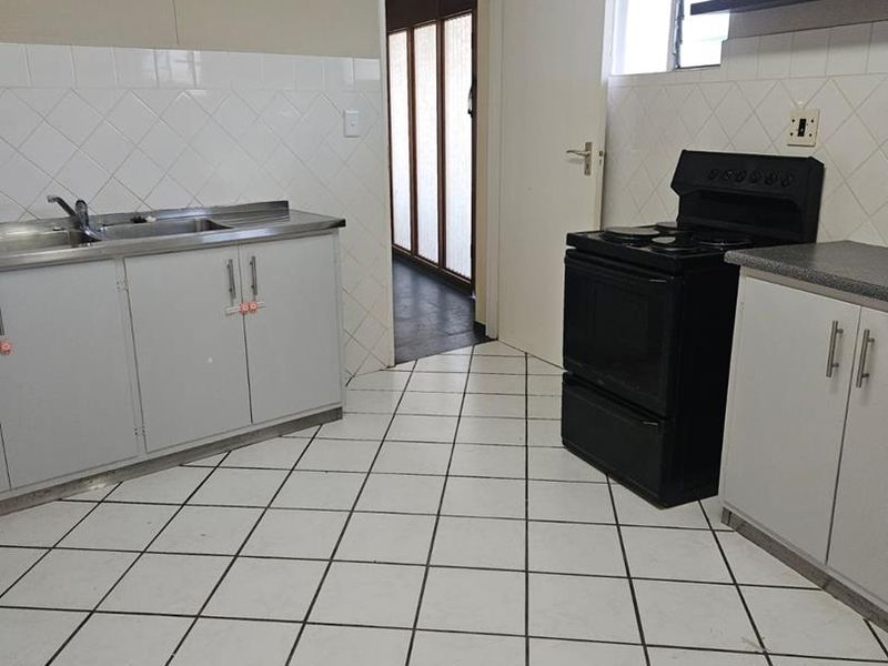 A functional kitchen featuring tiled flooring, a stainless steel sink, built-in cabinetry, and a freestanding stove, offering a clean space ready for updates.