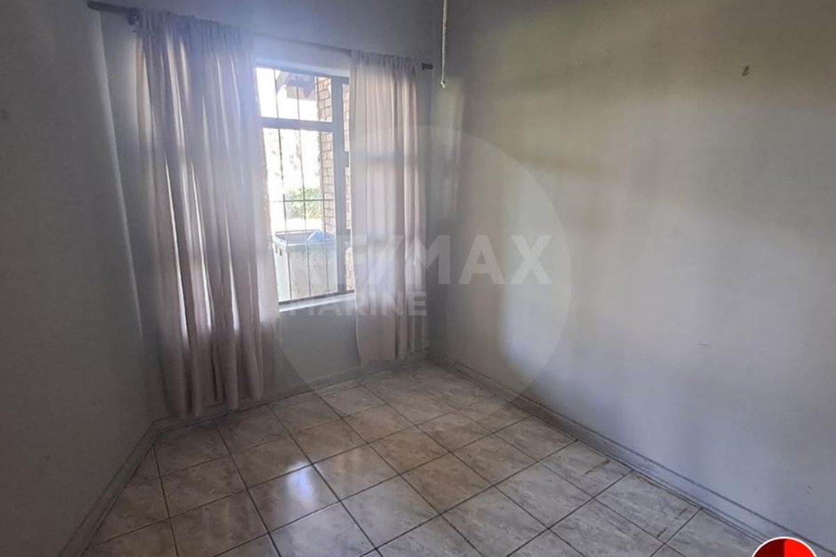 A vacant bedroom featuring tiled flooring and a window with security bars, offering a blank canvas for potential interior updates.