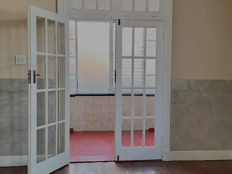 An empty living room featuring original hardwood flooring, tiled wainscoting, and classic French doors leading to an adjacent balcony area.
