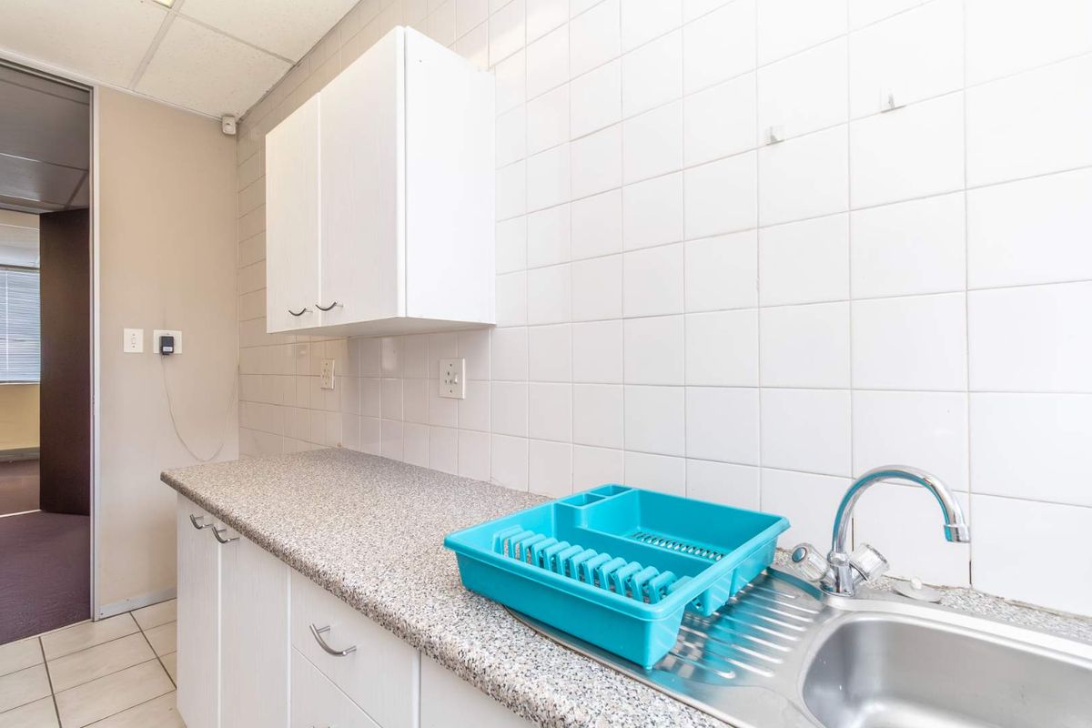 A functional office kitchenette featuring white cabinetry, a granite-look laminate countertop, and a stainless steel sink with a chrome mixer tap.