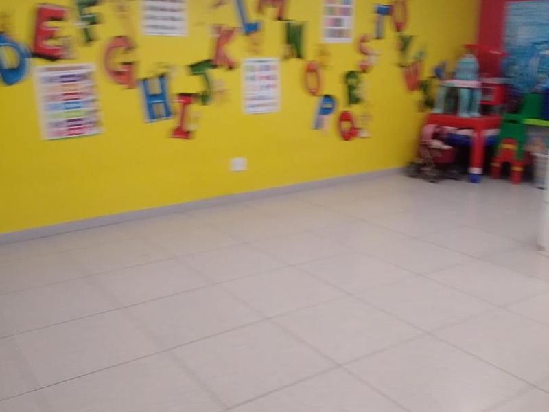 An open-plan interior space featuring tiled flooring and recessed ceiling lighting, currently utilized as a play area with bright yellow wall finishes.