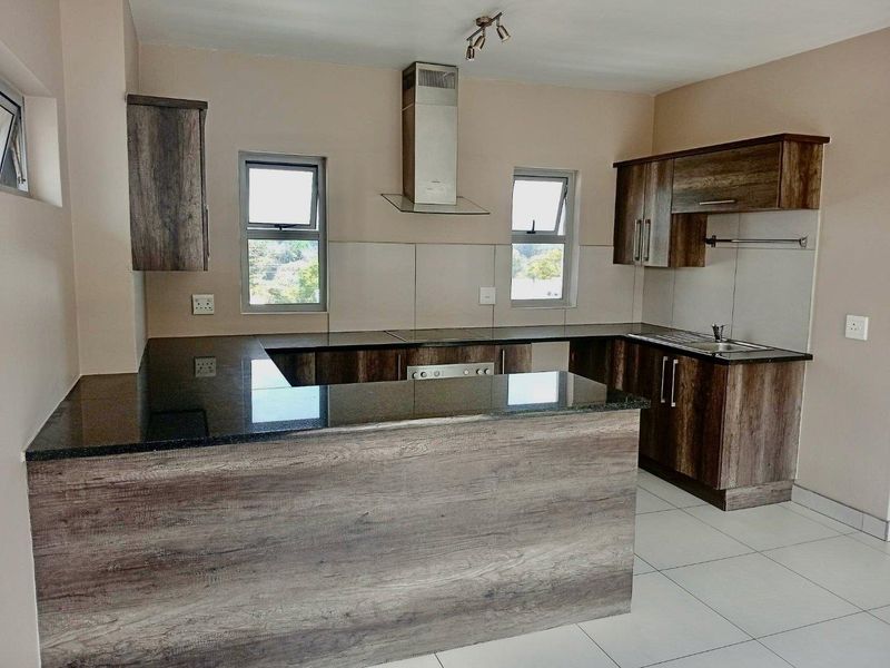 A modern, empty kitchen featuring wood-look cabinetry, granite countertops, a stainless steel extractor fan, and neutral tiled flooring.