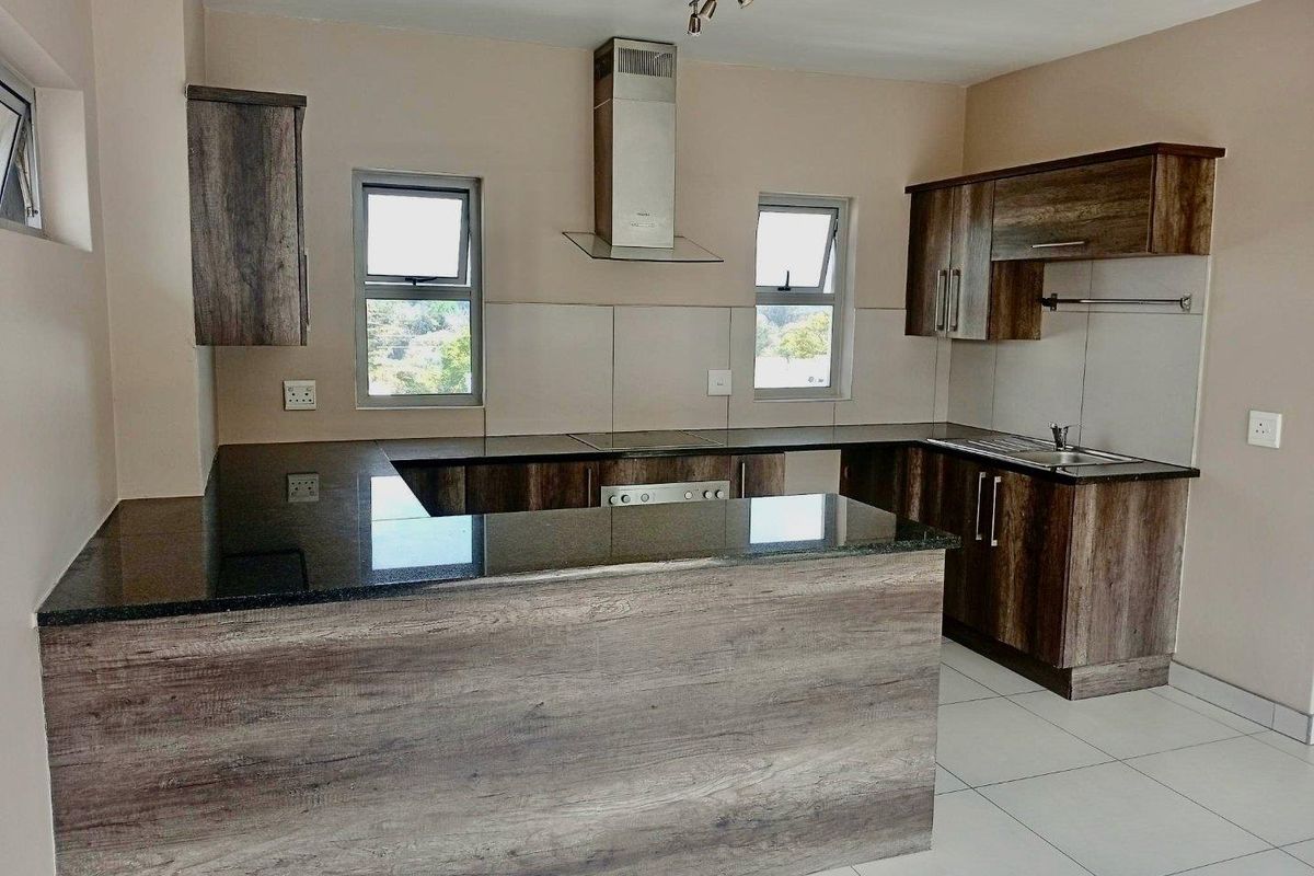 A modern, empty kitchen featuring wood-look cabinetry, granite countertops, a stainless steel extractor fan, and neutral tiled flooring.