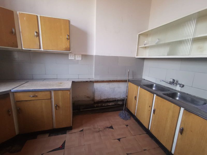 A dated kitchen featuring original laminate cabinetry, a double stainless steel sink, and tiled finishes, currently requiring renovation and cosmetic updates.