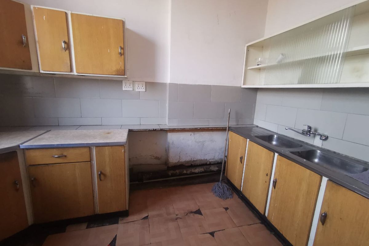 A dated kitchen featuring original laminate cabinetry, a double stainless steel sink, and tiled finishes, currently requiring renovation and cosmetic updates.