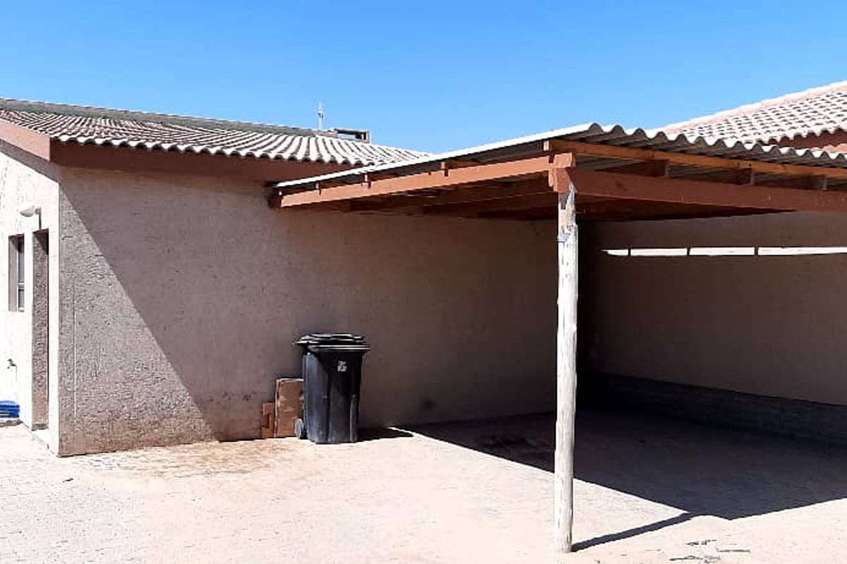 A rear exterior view of the property featuring a covered patio or carport area with a simple timber structure and corrugated roof.