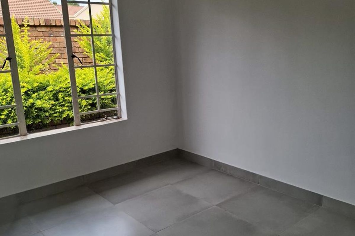 A bright, empty bedroom featuring neutral grey floor tiles and a large window with a view of the garden.