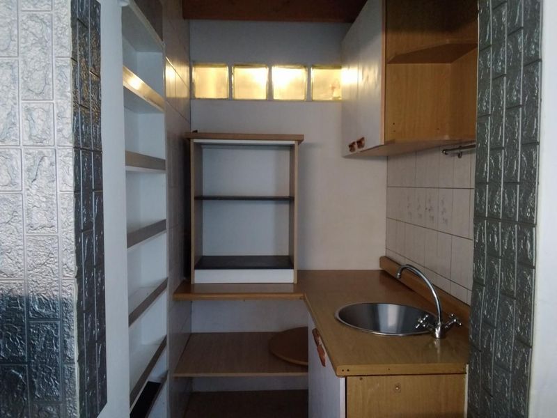 A compact scullery or utility area featuring built-in cabinetry, open shelving, a stainless steel sink, and a glass block window for natural light.