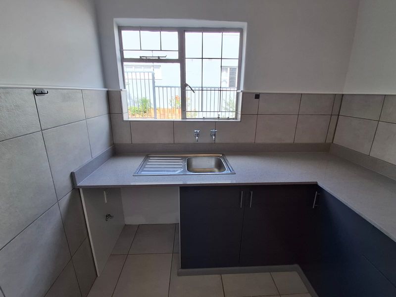 A clean, modern kitchen area featuring built-in cabinetry, a stainless steel sink, stone countertops, and neutral tiled finishes throughout.