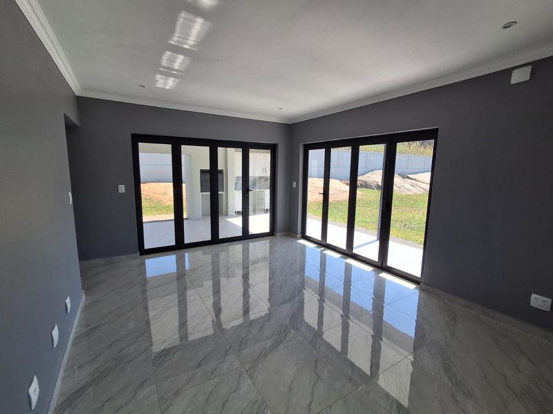 Spacious, modern living area featuring large format marble-look floor tiles, dark grey walls, and expansive black aluminium stacker doors opening to the garden.