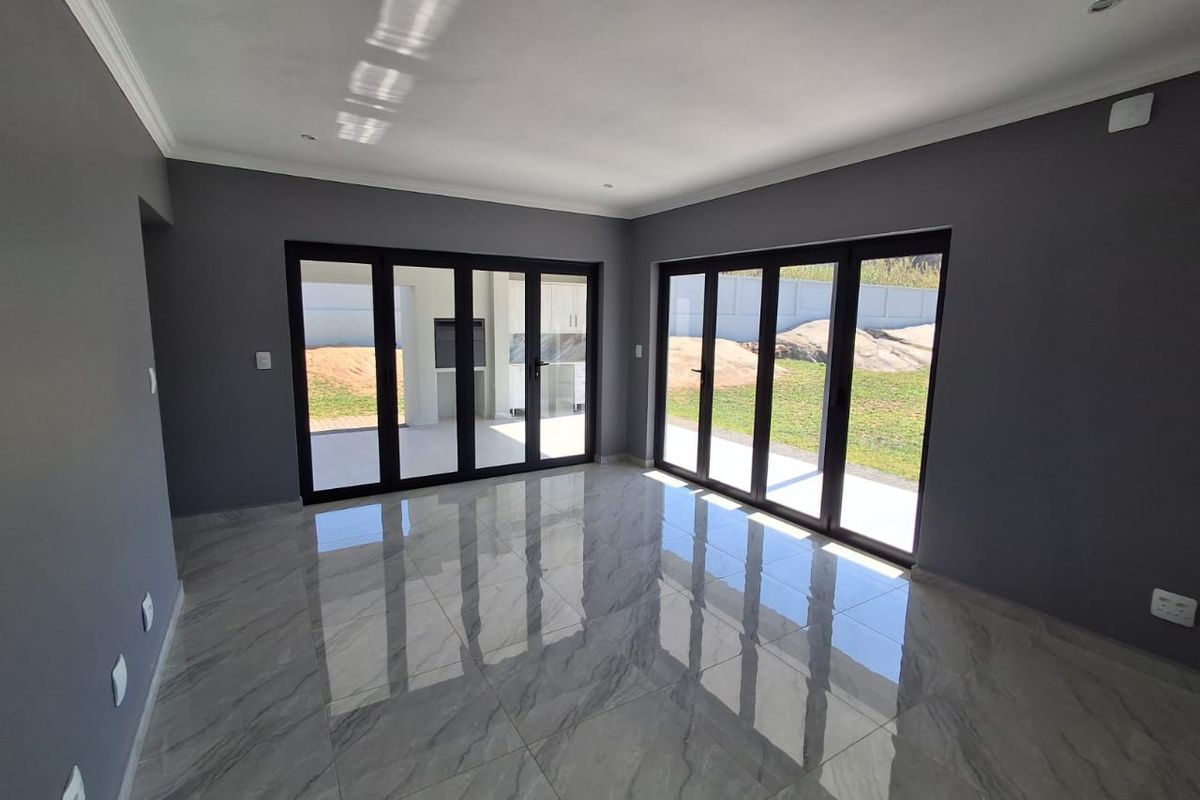 Spacious, modern living area featuring large format marble-look floor tiles, dark grey walls, and expansive black aluminium stacker doors opening to the garden.