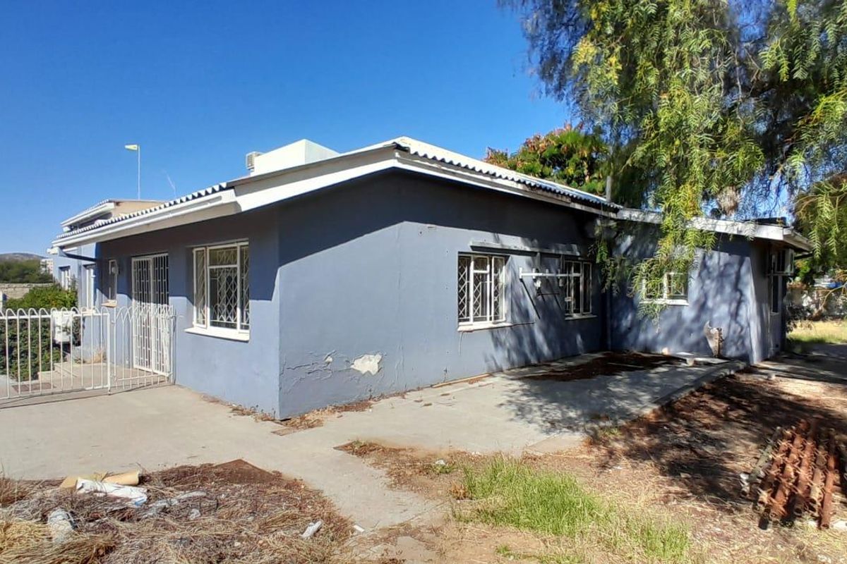 Rear exterior view of the property featuring a concrete patio area, security bars on windows, and a corrugated metal roof.