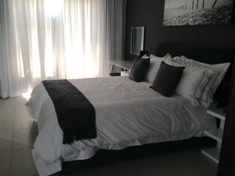 A well-lit bedroom featuring tiled flooring and floor-to-ceiling sheer curtains, creating a comfortable and private sleeping space.