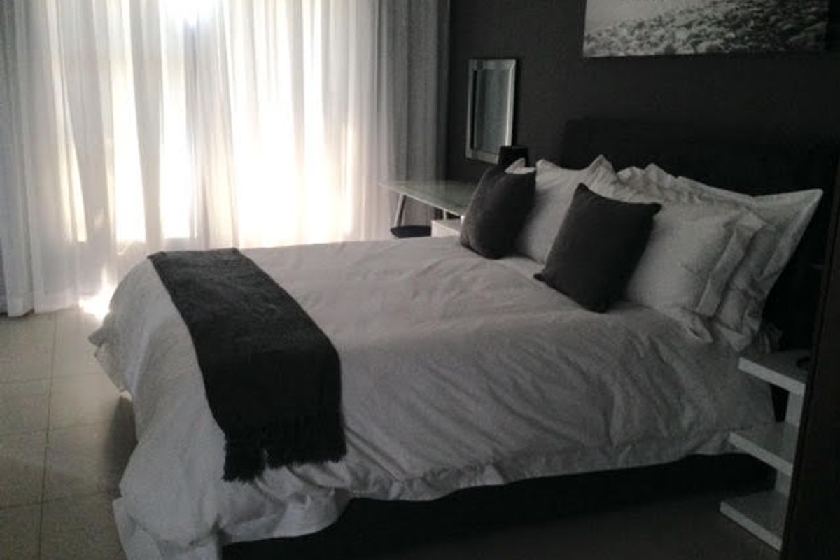 A well-lit bedroom featuring tiled flooring and floor-to-ceiling sheer curtains, creating a comfortable and private sleeping space.