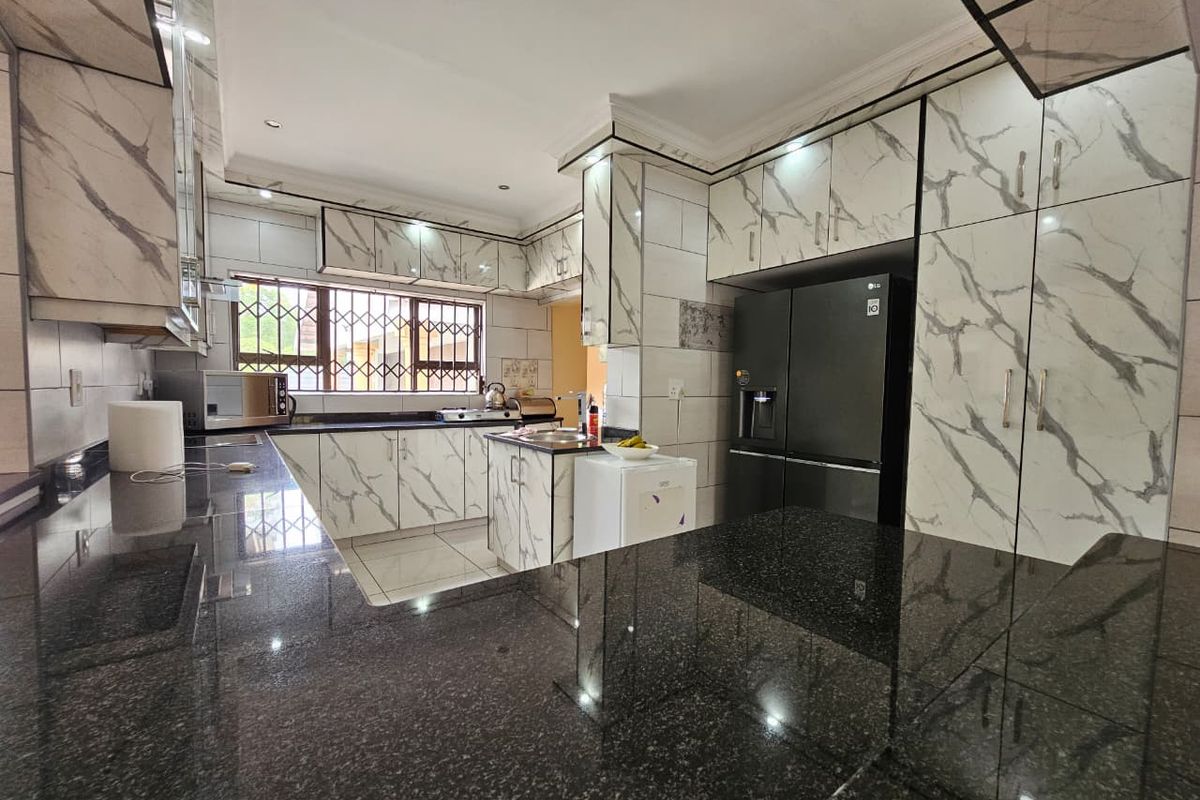 A modern kitchen featuring marble-effect cabinetry, dark granite countertops, and integrated storage space with tiled flooring and security bars on the windows.