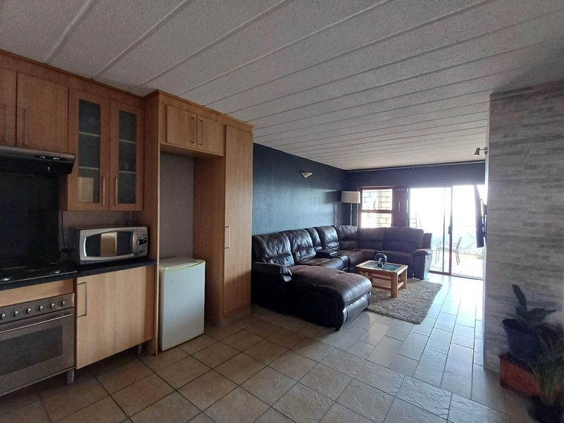 Open-plan living area featuring a functional kitchen with built-in cabinetry, tiled flooring, and sliding doors leading to an outdoor space.